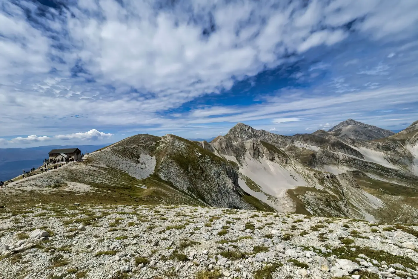 Breathtaking view of rugged mountains and a secluded cabin under a blue sky.
