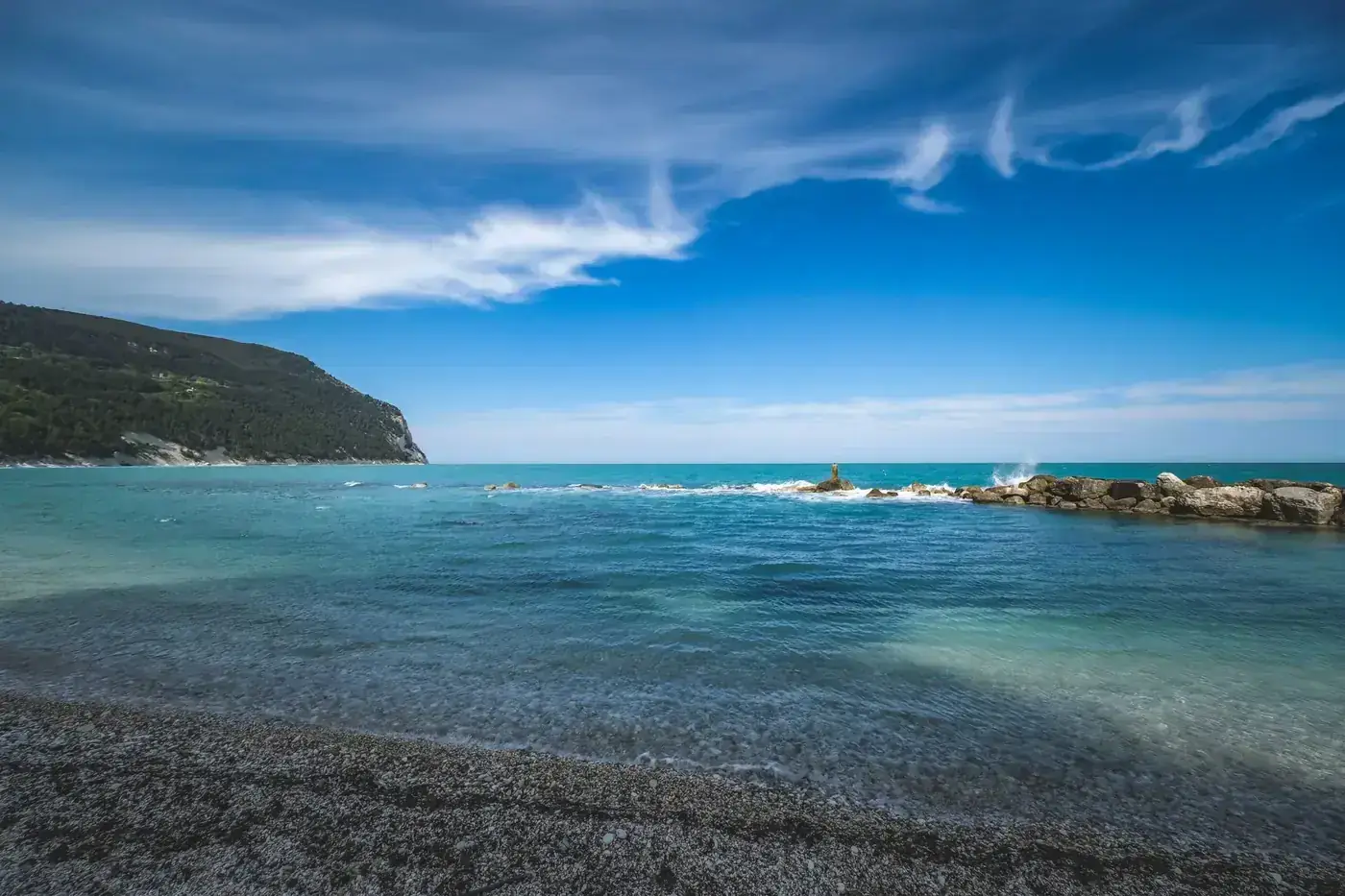 A serene beach scene featuring clear blue water and a rocky coastline under a bright blue sky.