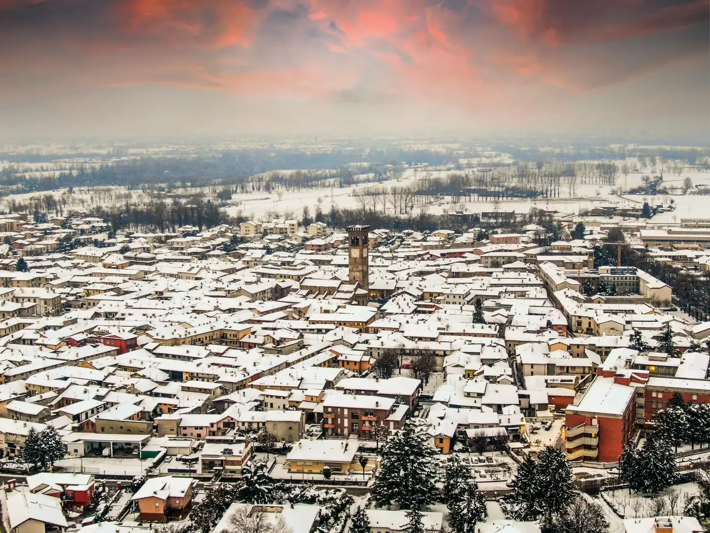 Aerial view of snowy rooftops in Rivolta d'Adda, Lombardy under vibrant winter skies.