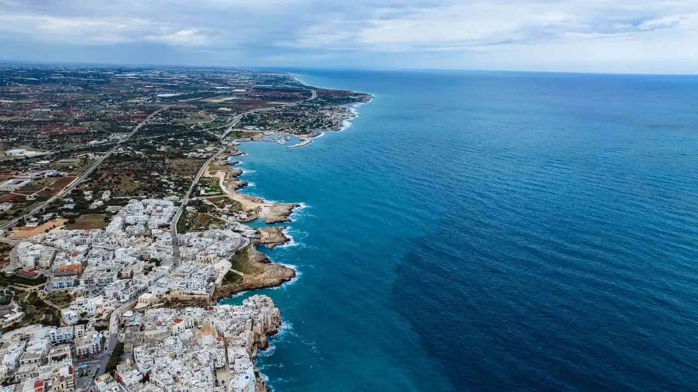 Breathtaking aerial view of Polignano a Mare's coastline in Italy, showcasing vibrant blue waters and summer vibes.