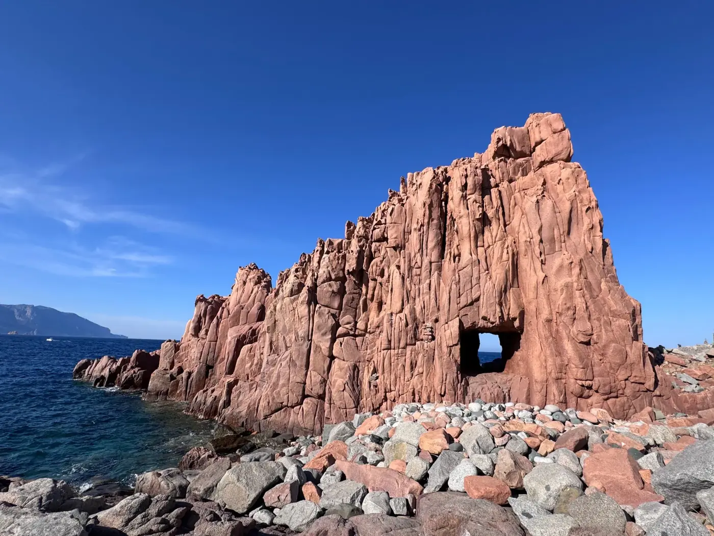 Stunning view of towering red rock formations along Sardinia's pristine coastline under a clear blue sky.