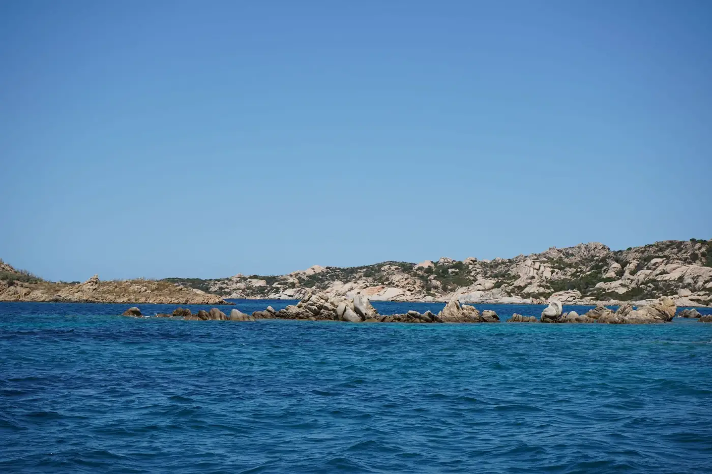 Discover Sardinia's rocky coastline and vibrant emerald waters under a clear blue sky.