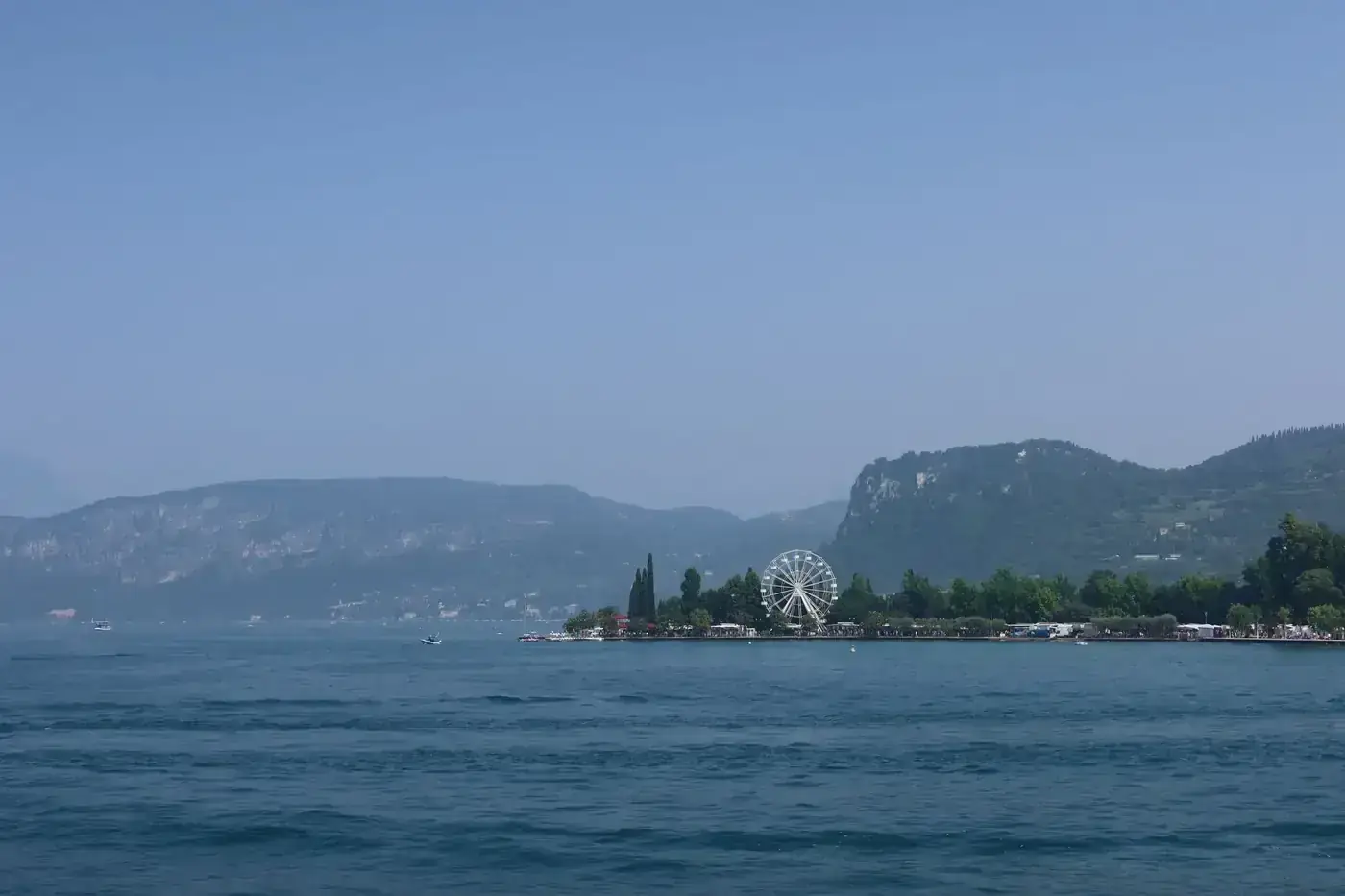Serene landscape of Lake Garda featuring a distant Ferris wheel and lush greenery.