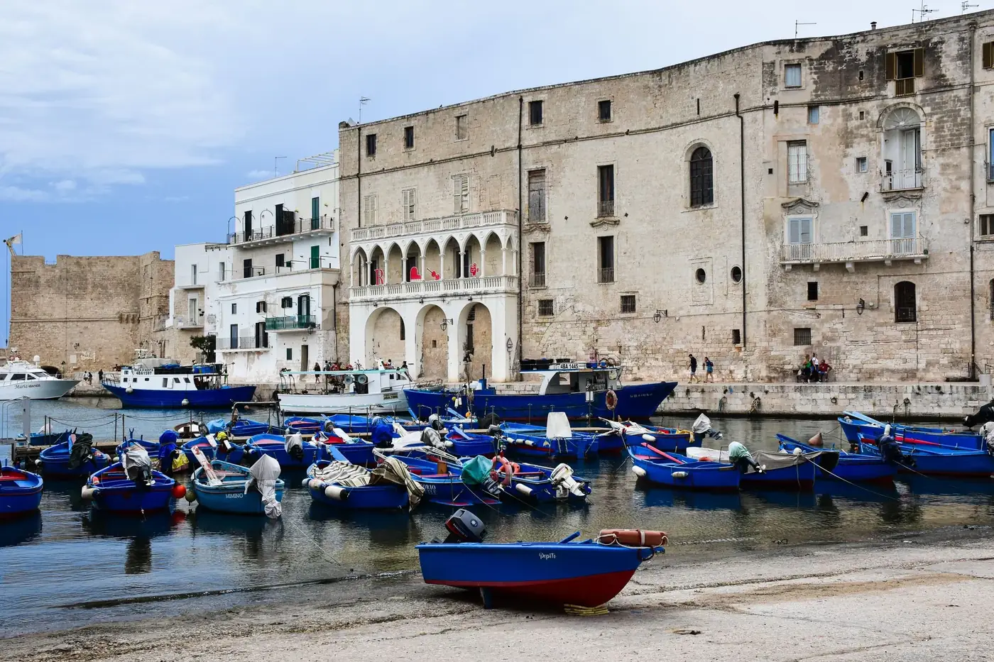 Colorful fishing boats docked in Monopoli's harbor, surrounded by historic architecture, Apulia, Italy.