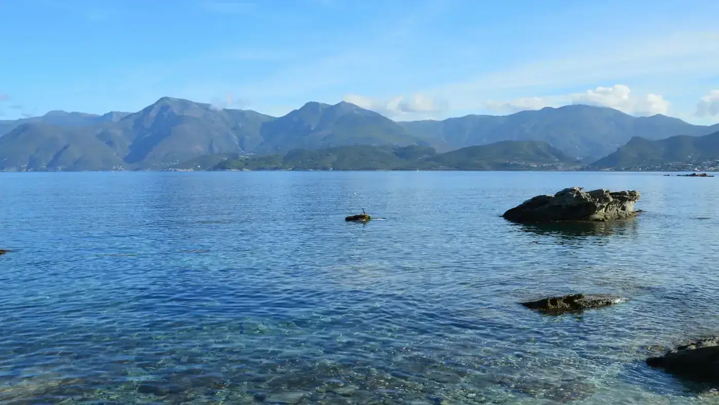 Calm sea with clear water and rocky coastline under a blue sky in Patrimonio, Corse, France.