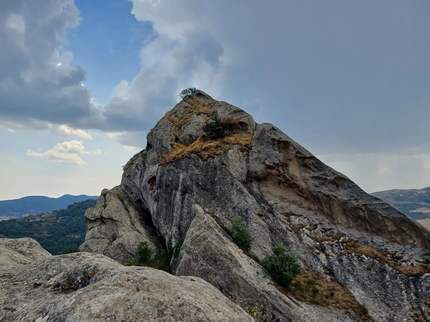 Dramatic rocky peak under cloudy sky in Castelmezzano, Italy, showcasing rugged landscape.