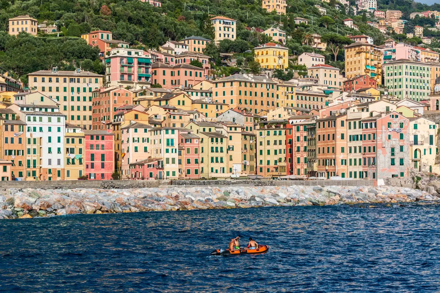 Lively scene of colorful buildings by the sea in Camogli, Liguria, with people rowing.