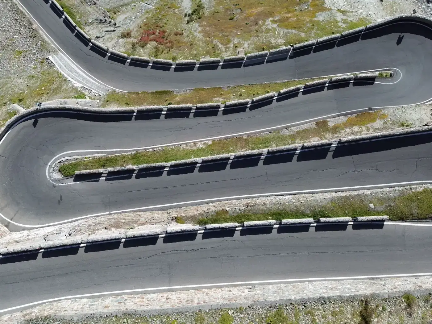 Aerial shot of winding mountain road in the Alps, showcasing switchbacks and rugged terrain.