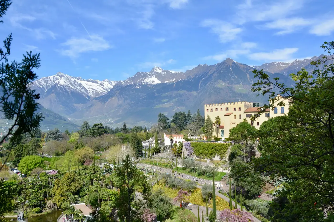 Stunning spring view of Merano, Italy with lush gardens and snow-capped mountains.