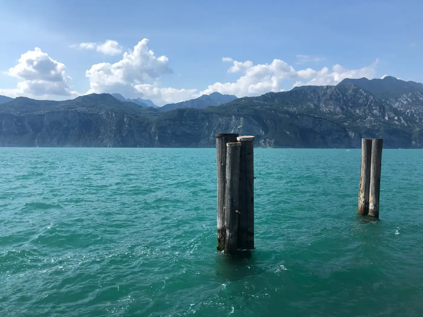 A tranquil scene of Lake Garda's turquoise waters with mountain views and wooden pilings.