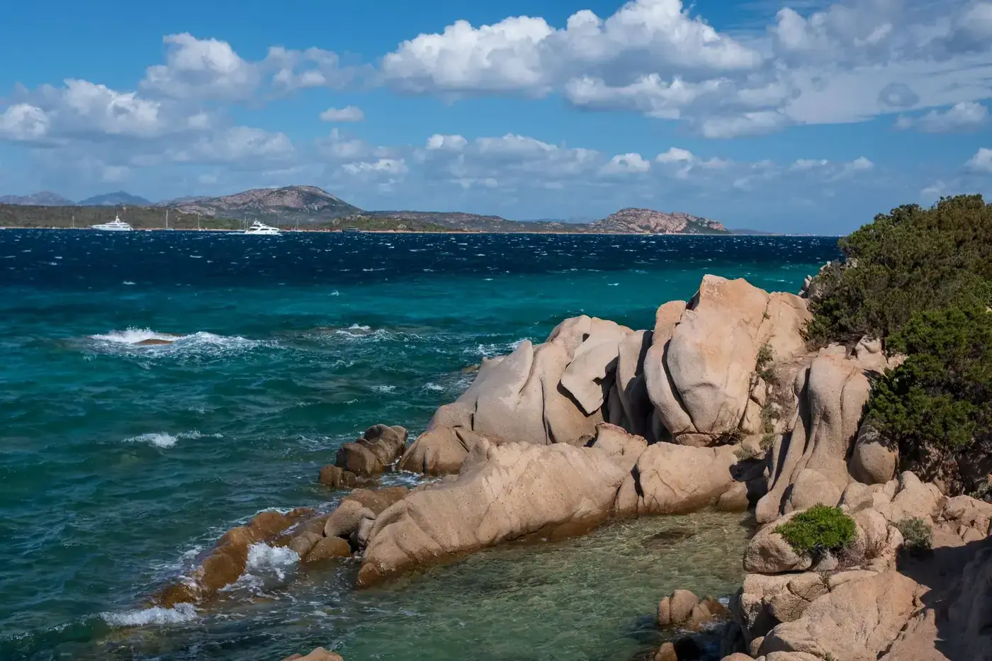 Scenic coastal rocks and turquoise sea in Sardinia, Italy under a bright, cloudy sky.