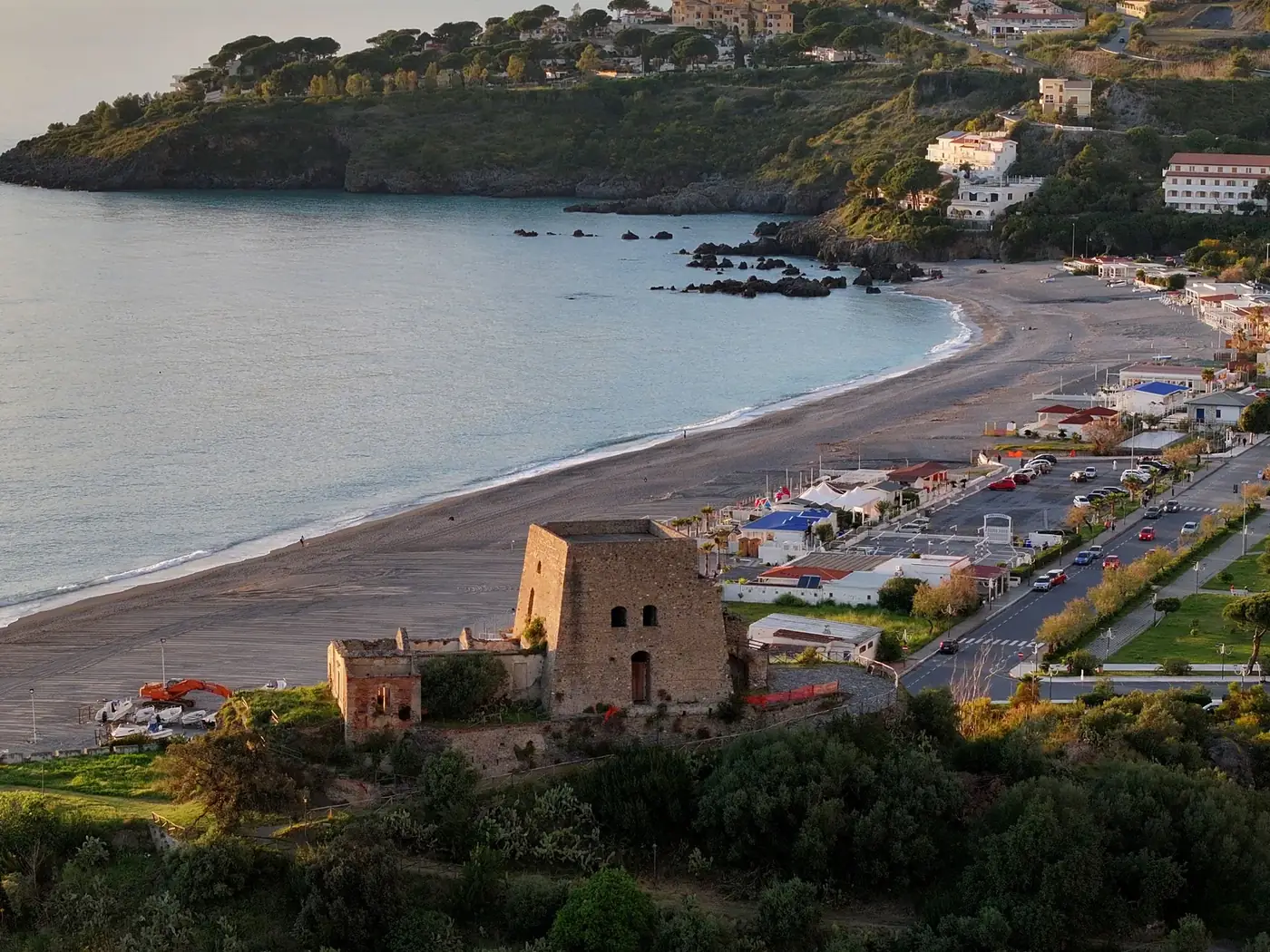 Aerial view of a coastal beach and historic ruins at sunset, featuring stunning natural beauty.