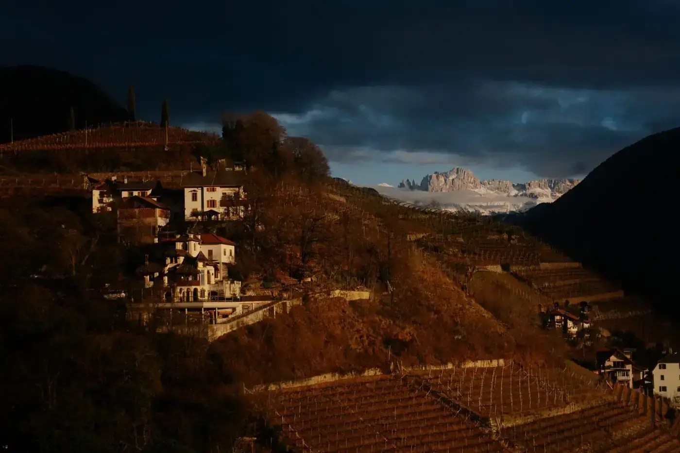 Picturesque village on a hill with dramatic mountains in twilight.