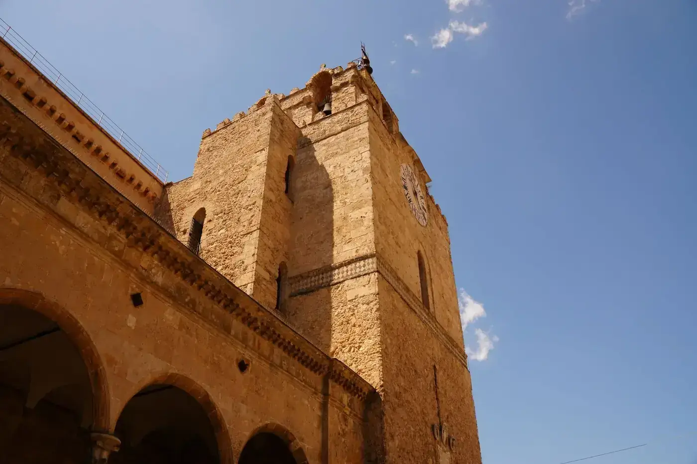Wide-angle view of Monreale Cathedral's historic bell tower against a vivid blue sky in Sicily, Italy.