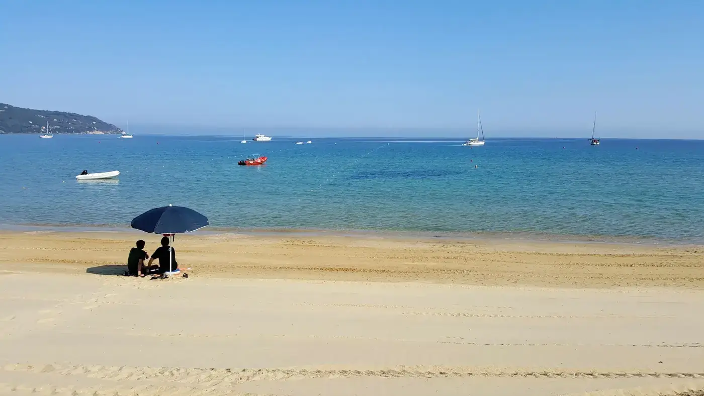 Serene beach view on Elba Island, Tuscany, with umbrella and boats.