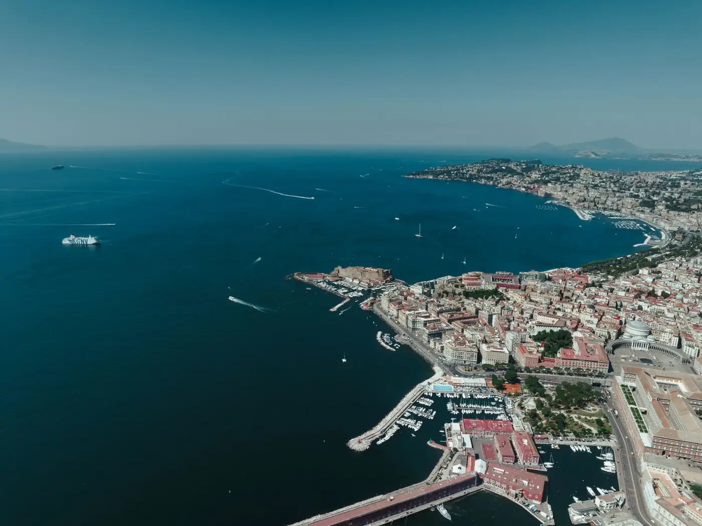 A stunning aerial view showcasing the vibrant city of Napoli, its bustling harbor, and the scenic Mediterranean coastlin