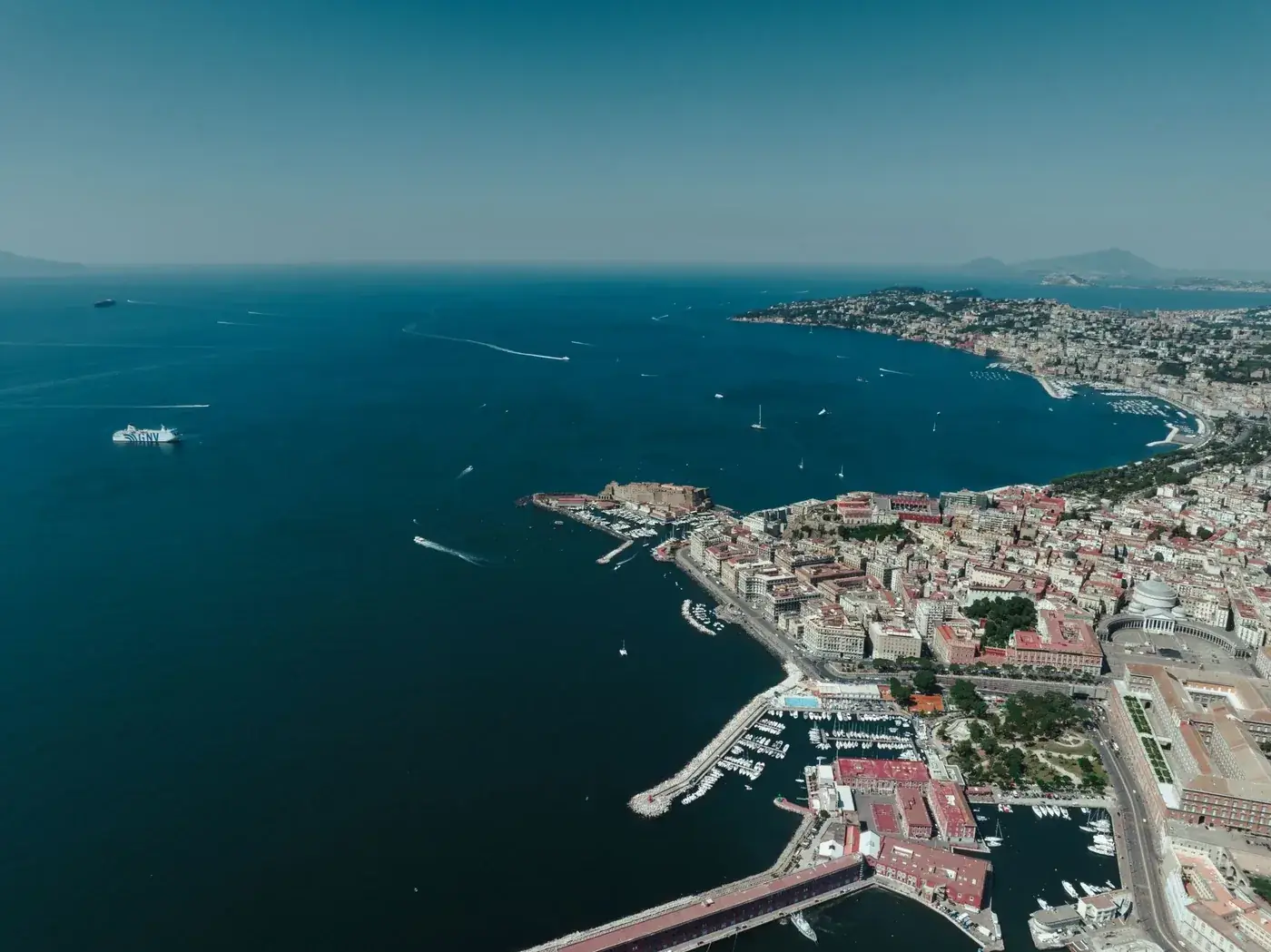 A stunning aerial view showcasing the vibrant city of Napoli, its bustling harbor, and the scenic Mediterranean coastline.