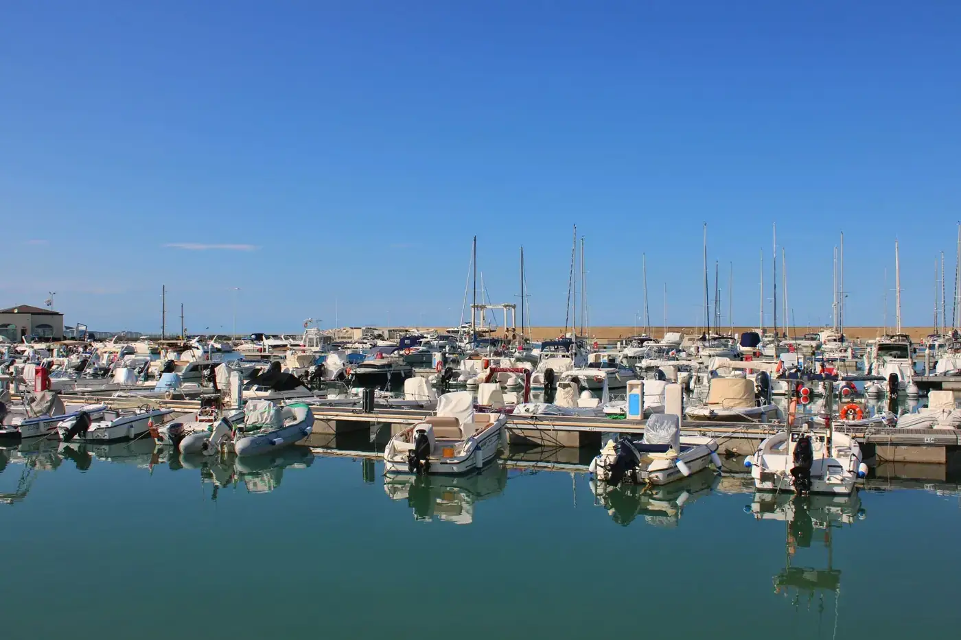 Boats docked in a serene marina in Montenero di Bisaccia, Italy, under clear blue skies.