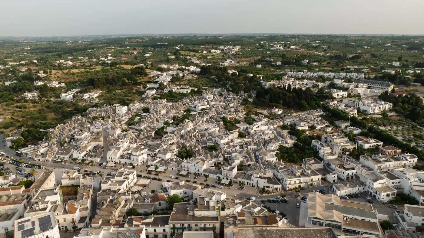 Panoramic aerial shot of Alberobello's iconic trulli houses surrounded by lush greenery.