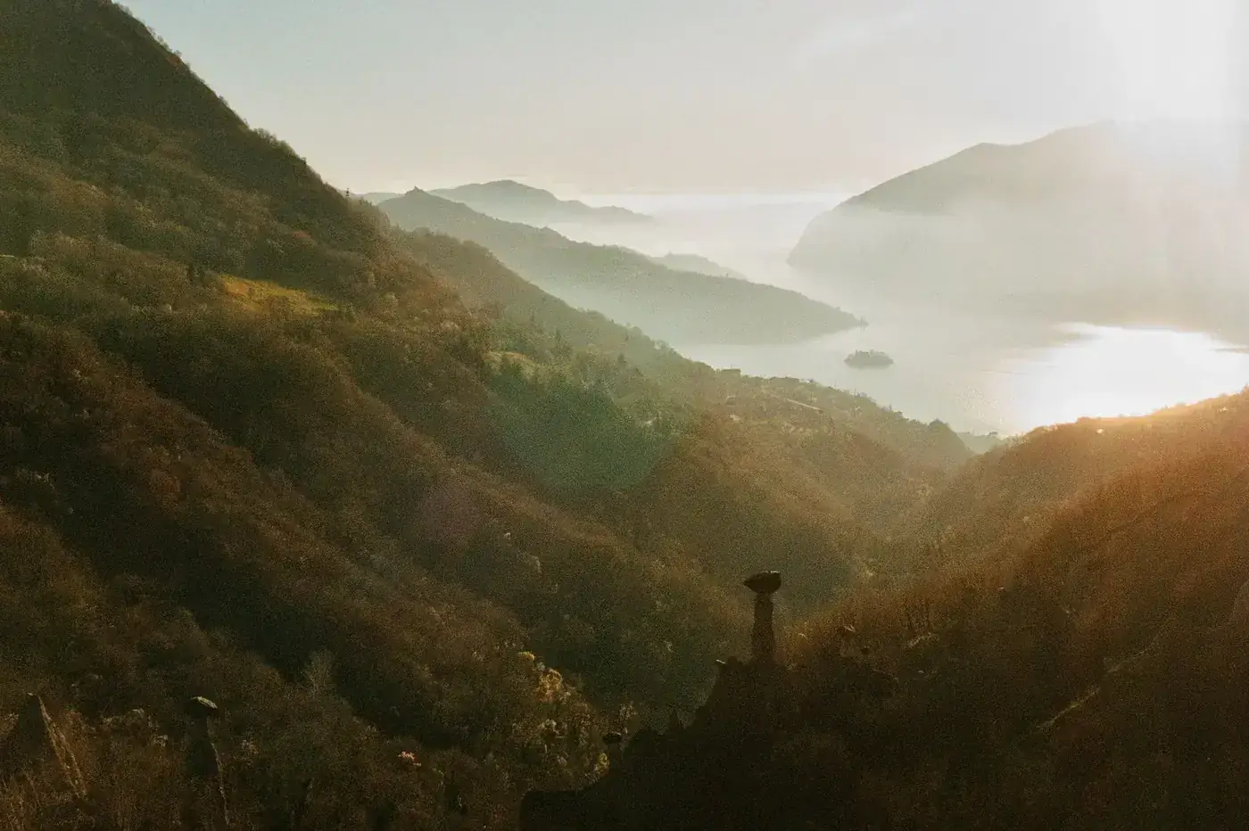 A picturesque valley in Italy enveloped in sunlight and mist, showcasing serene natural beauty.