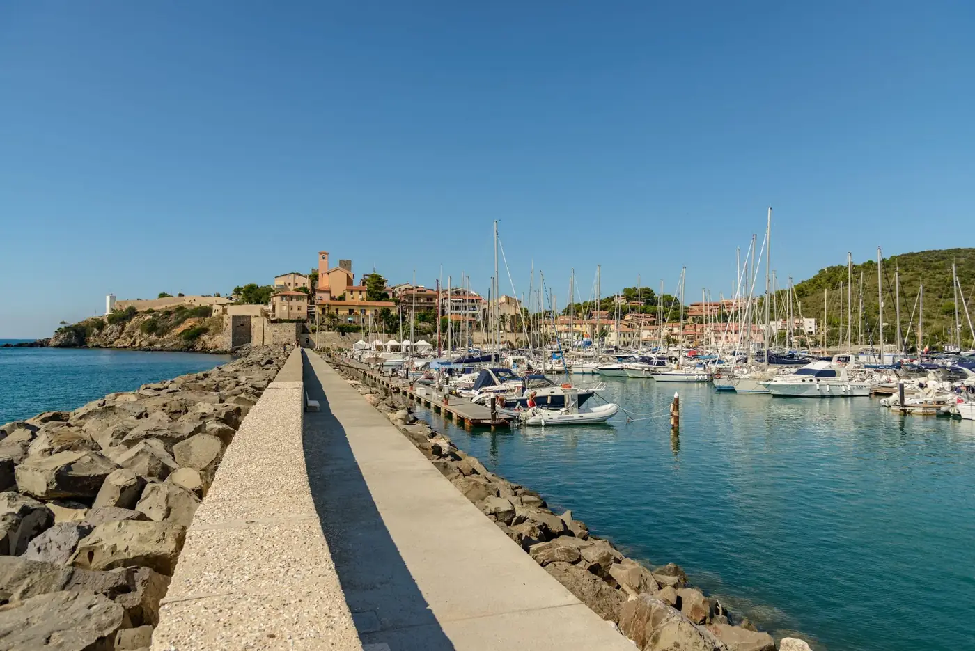Beautiful marina with sailboats near a picturesque coastal village under clear blue skies.