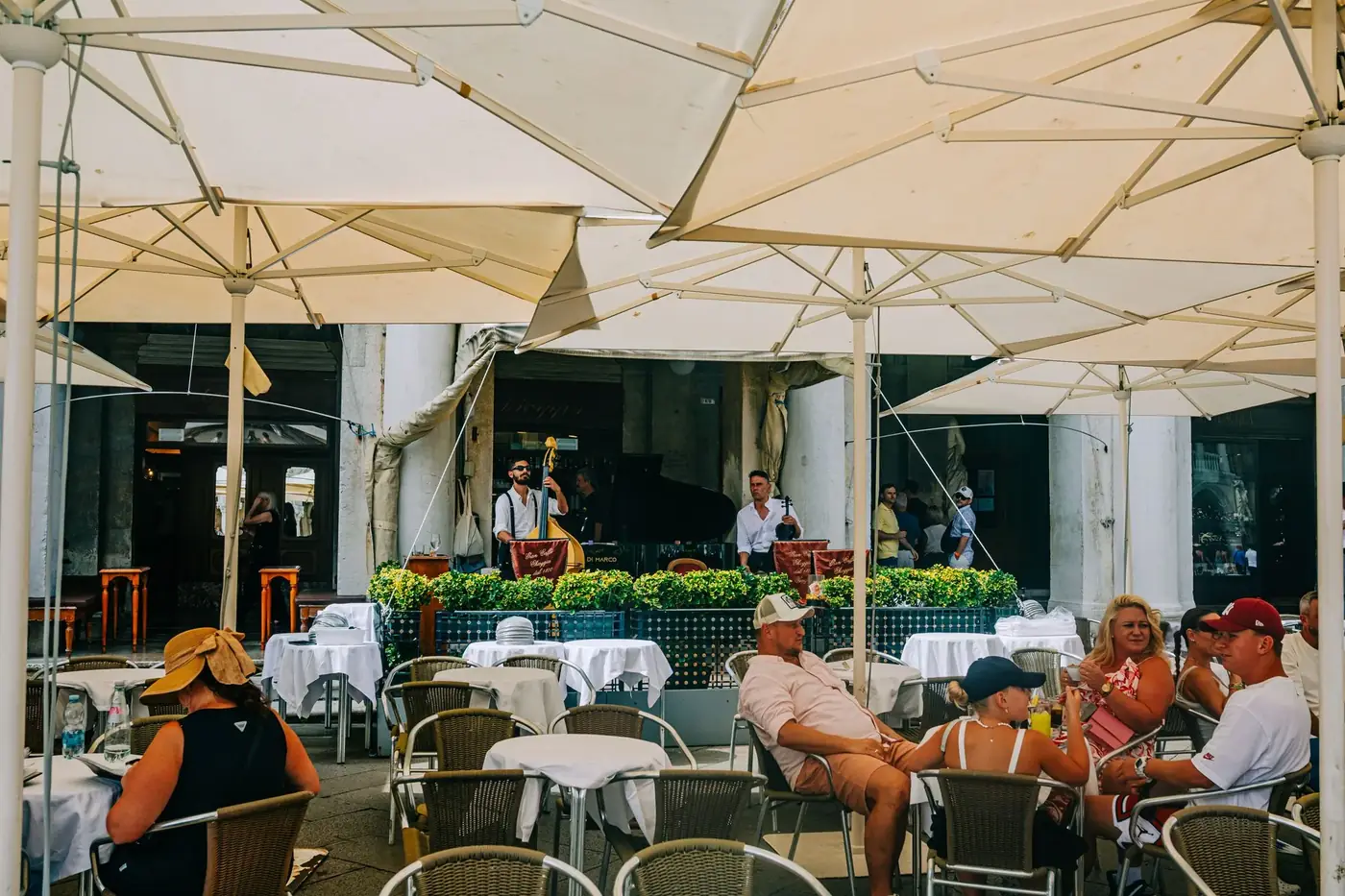 Lively outdoor cafe scene featuring diners and musicians under umbrellas on a warm summer day.