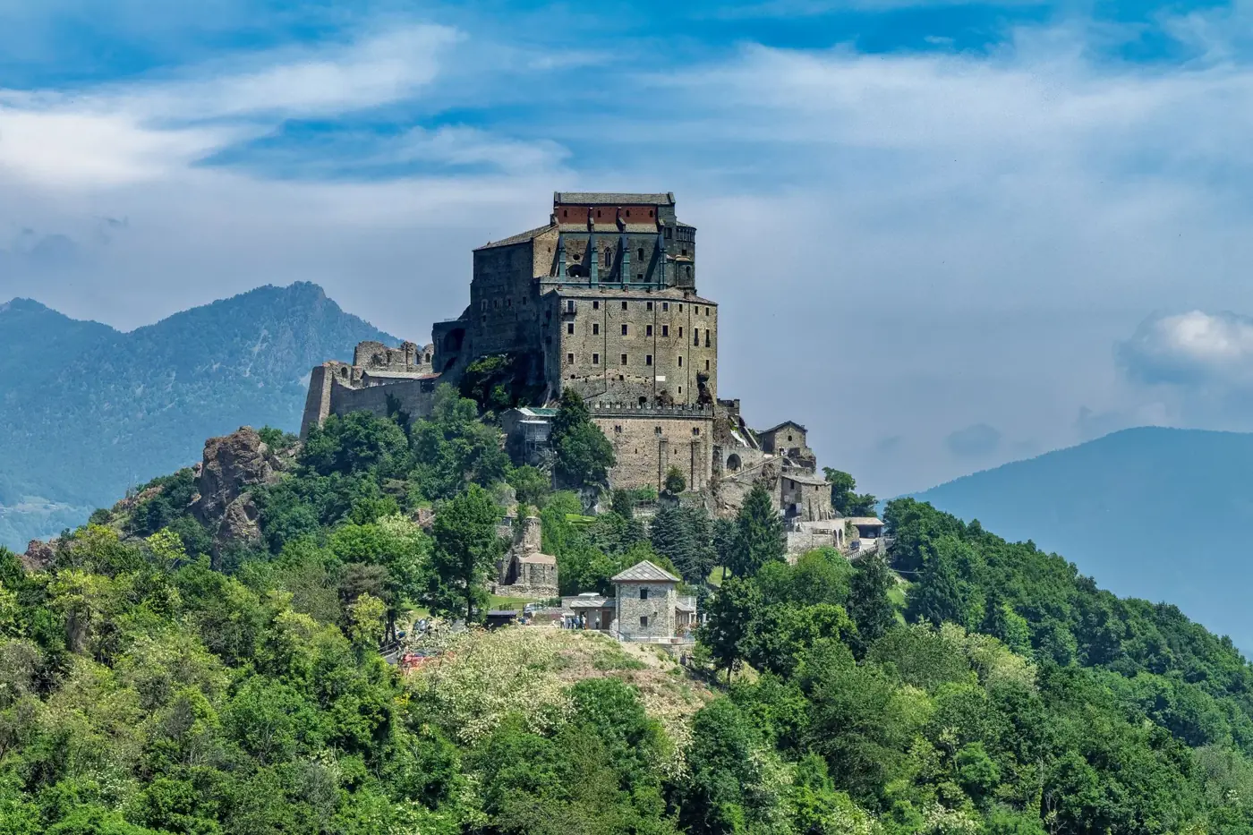 A stunning view of the Sacra di San Michele Abbey perched on a hill in Piemonte, Italy, surrounded by lush greenery.