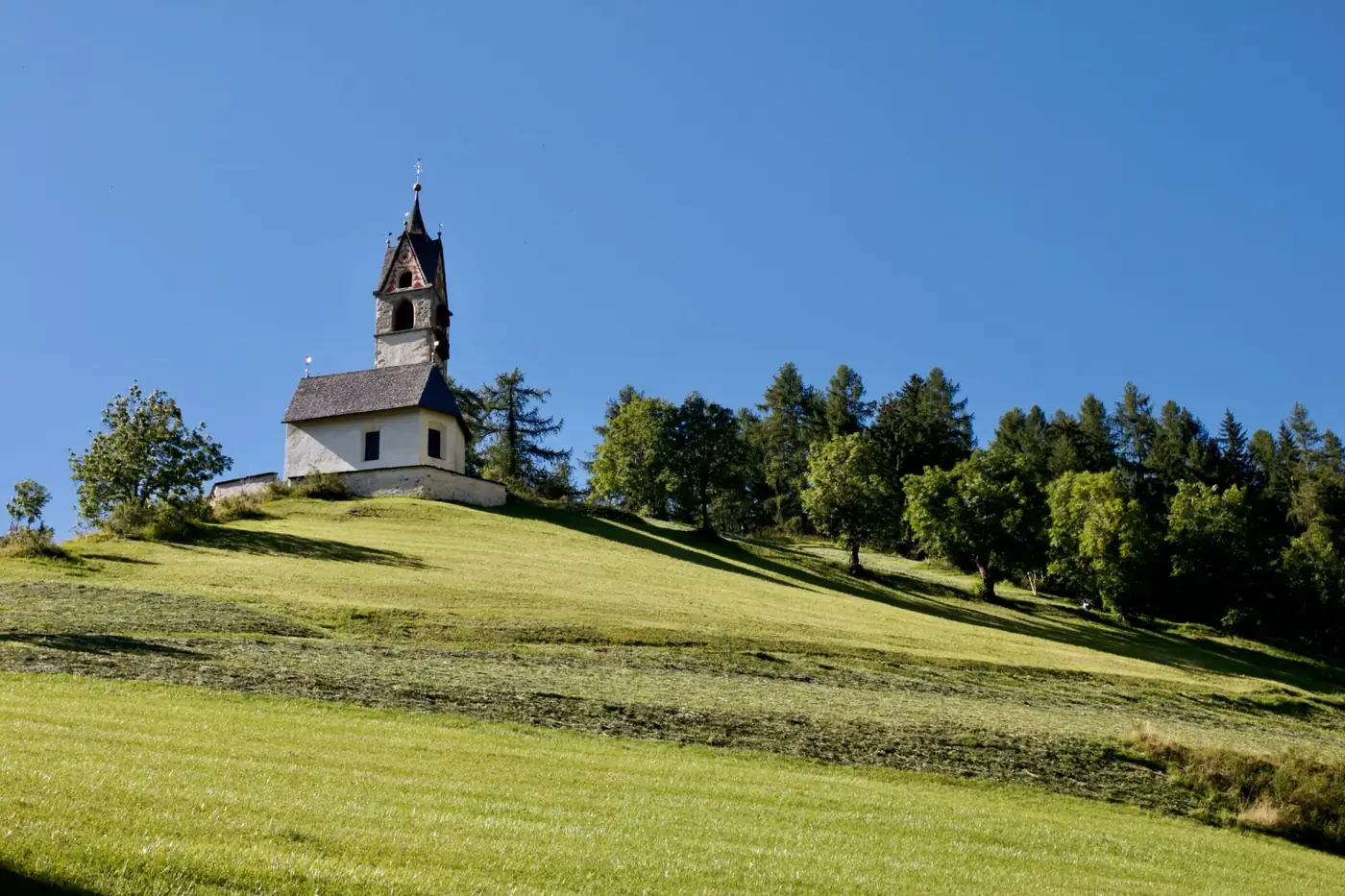 Idyllic landscape with St Barbara Church on a hilltop in Trentino-Alto Adige under clear blue skies.
