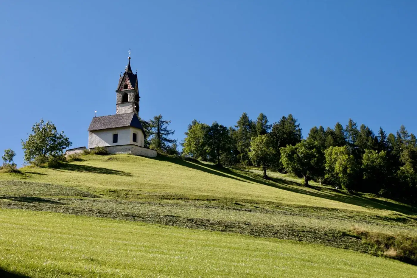 Idyllic landscape with St Barbara Church on a hilltop in Trentino-Alto Adige under clear blue skies.