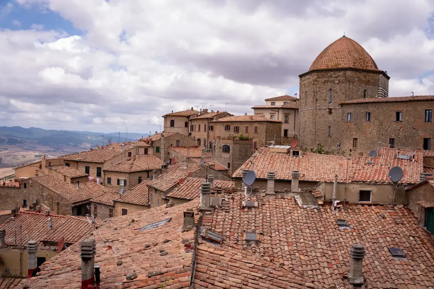 Explore the picturesque rooftops of a historic Italian village under a canvas of clouds.