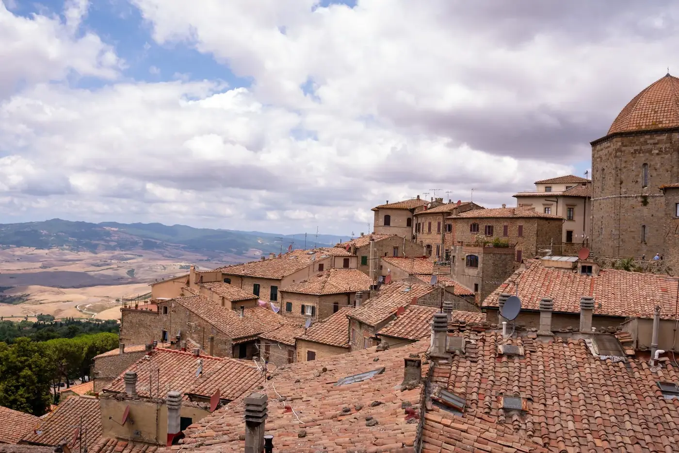 A stunning view of traditional Italian rooftops with a beautiful countryside backdrop under a cloud-filled sky.