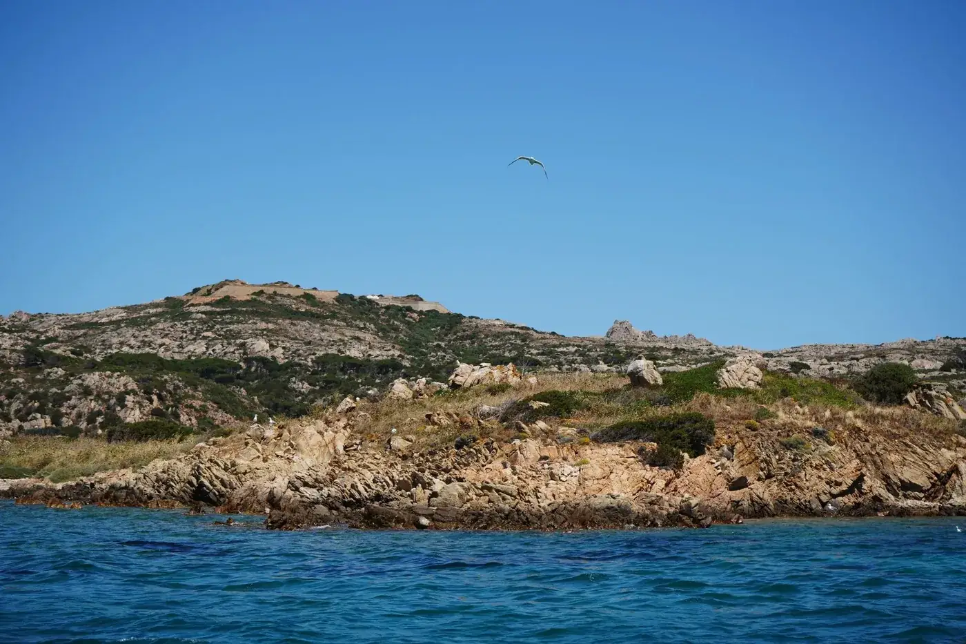Breathtaking rocky coastline of Sardinia, Italy with clear skies and tranquil ocean waters.