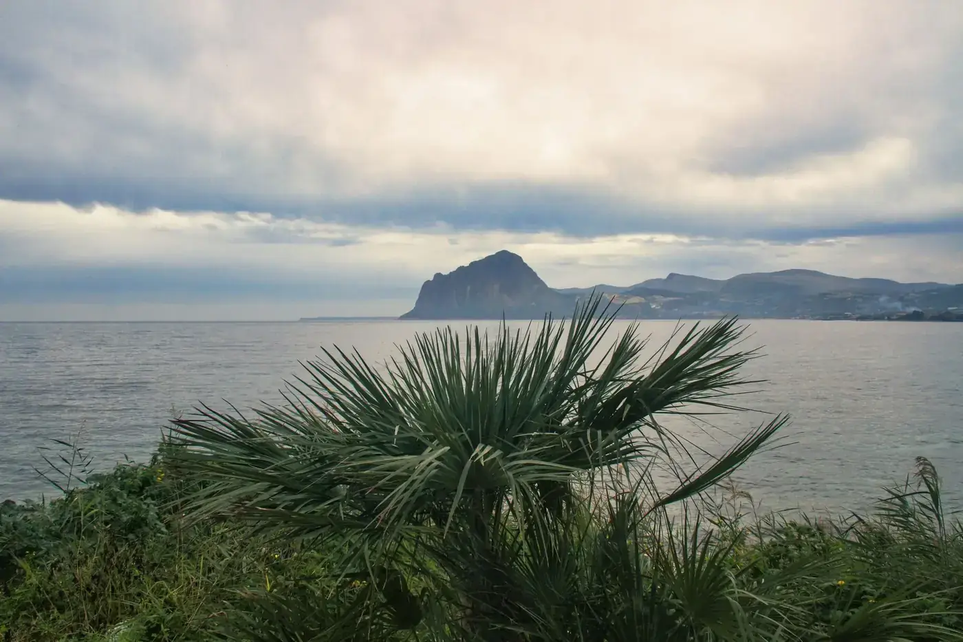 Scenic view of Monte Cofano from Sicilia's coast with lush greenery and calm sea.