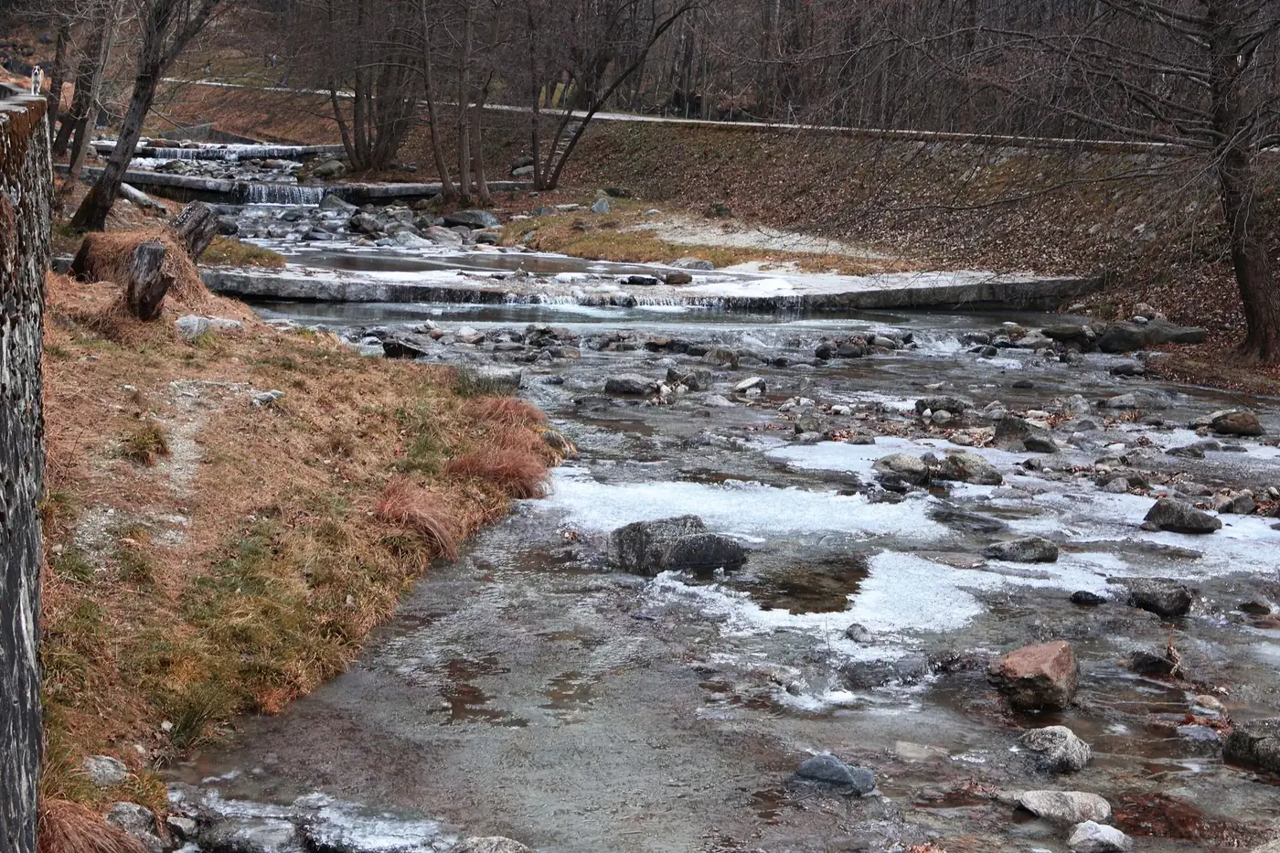 Peaceful winter scene of a partially frozen stream in Chiavenna, Italy, showcasing nature's beauty.