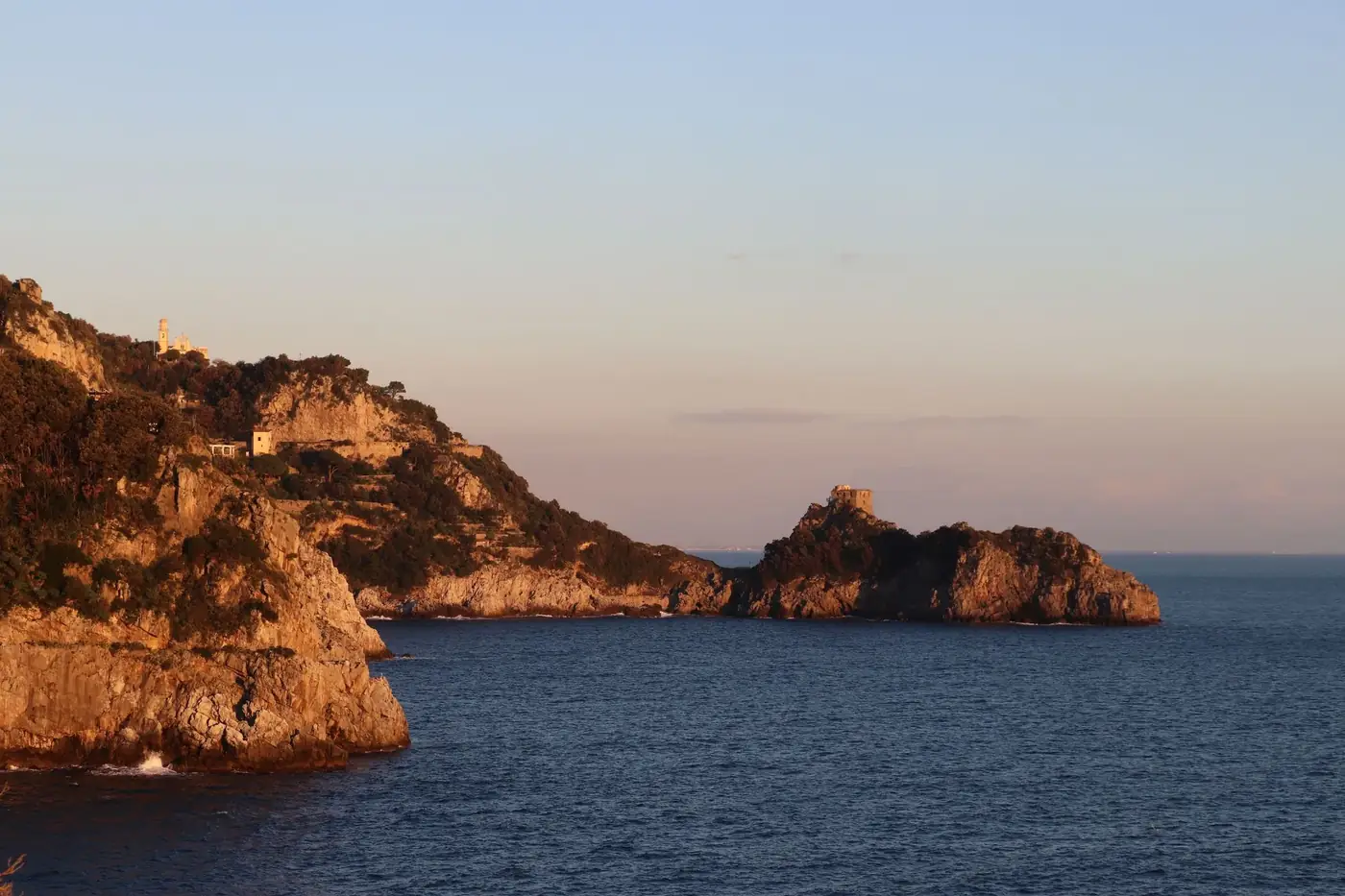 Dramatic cliffs meet tranquil sea at Praiano's coastline during sunset.