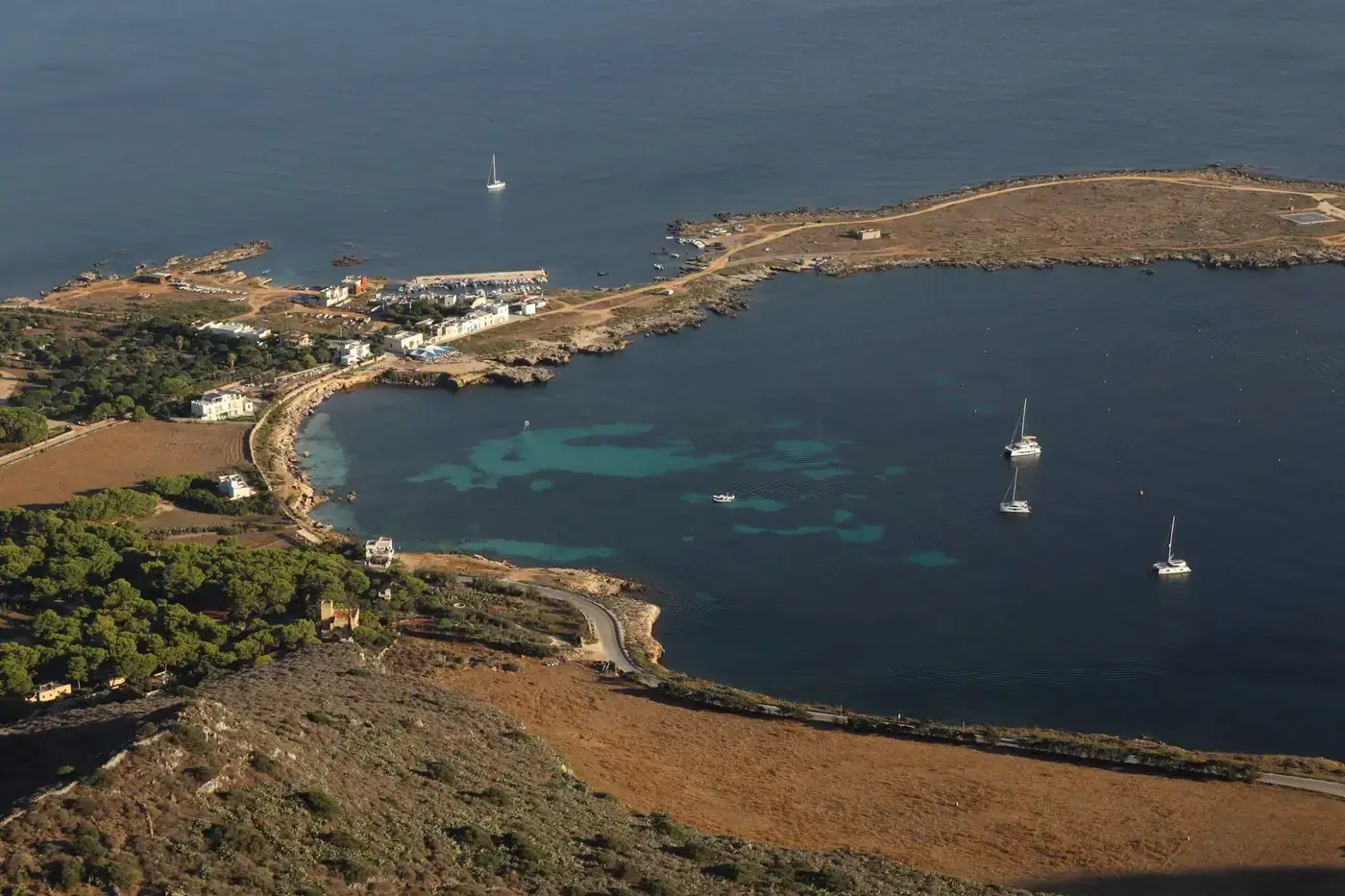 Stunning aerial view of a coastal harbor in Sicilia, Italy with sailboats and clear waters.