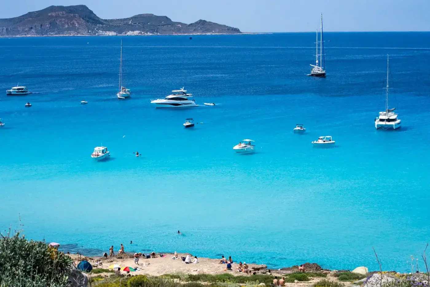 Idyllic view of Sicily's turquoise sea with yachts and beachgoers on a sunny summer day.