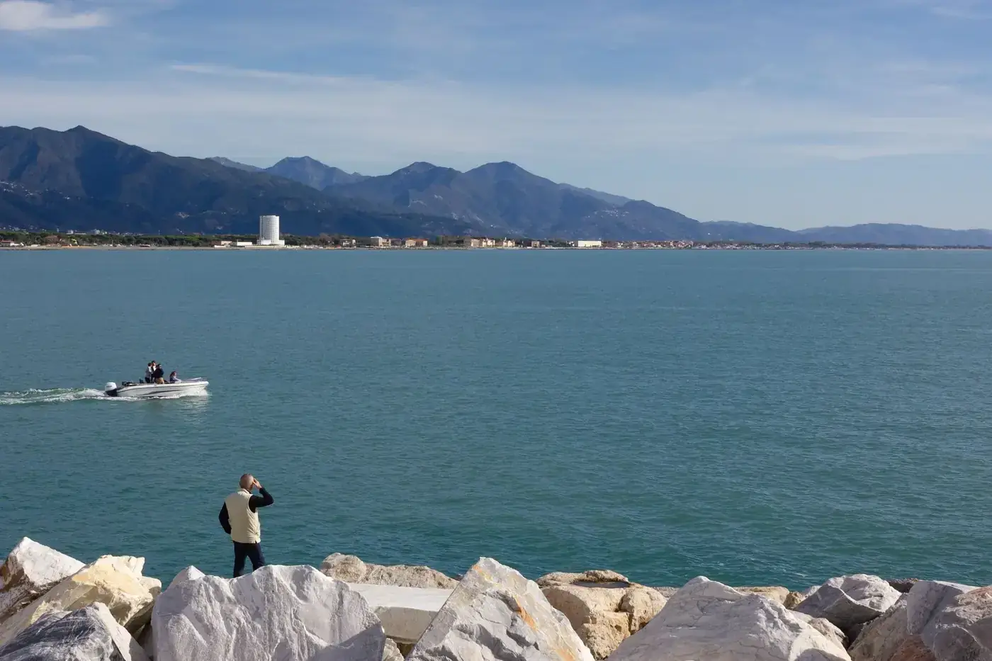 A man enjoys the view of a motorboat on a scenic coastal landscape with mountains in the background.
