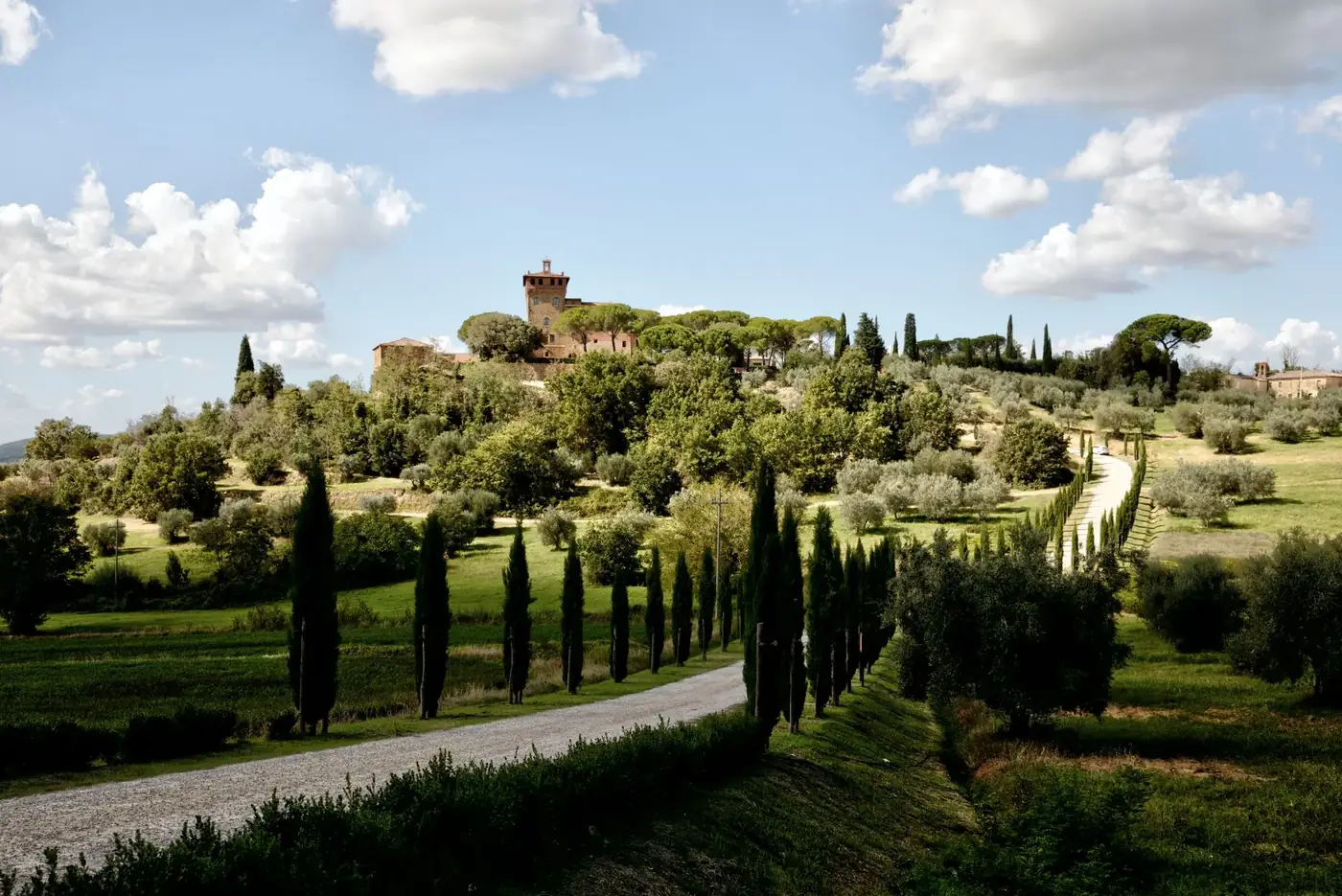 Beautiful Tuscany countryside with a historic castle and cypress-lined roadway under a bright sky.