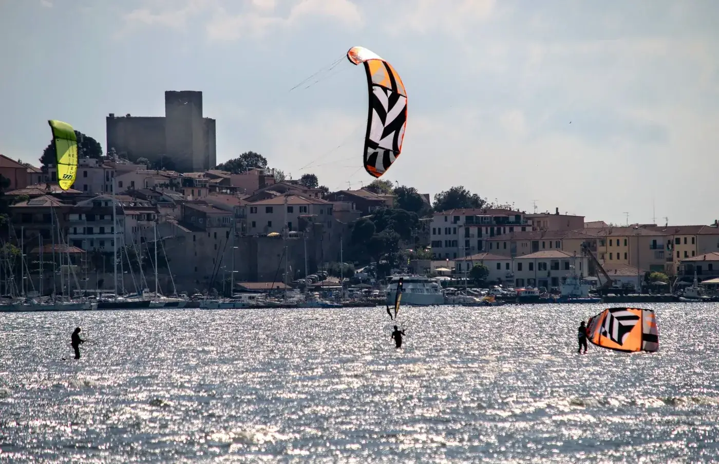 Kitesurfers navigating waves near a charming coastal town under a cloudy sky.
