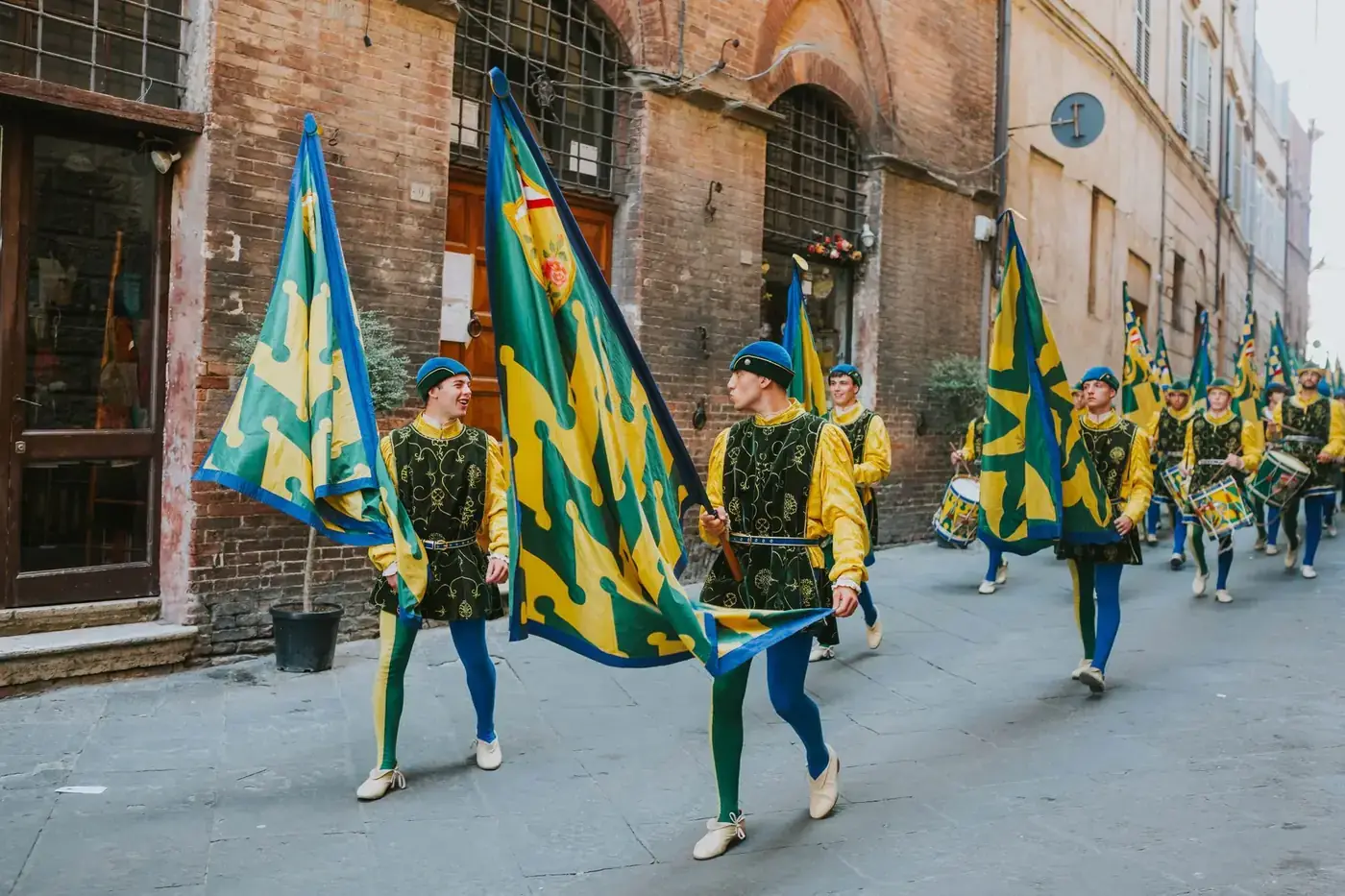 Colorful medieval parade with costumed flag bearers marching in a historic Italian street.