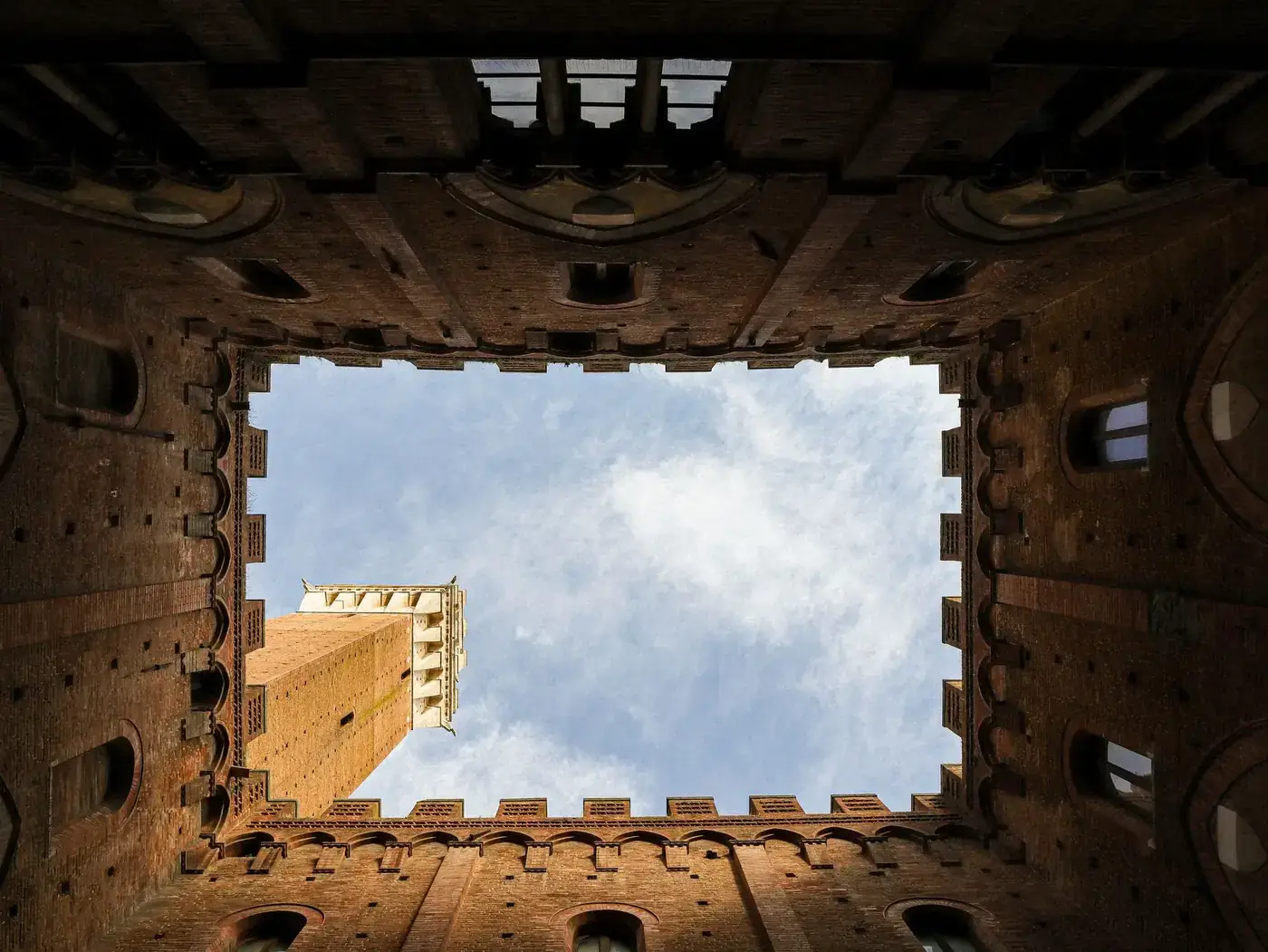Captivating view from below of a medieval tower surrounded by brick walls against a blue sky.