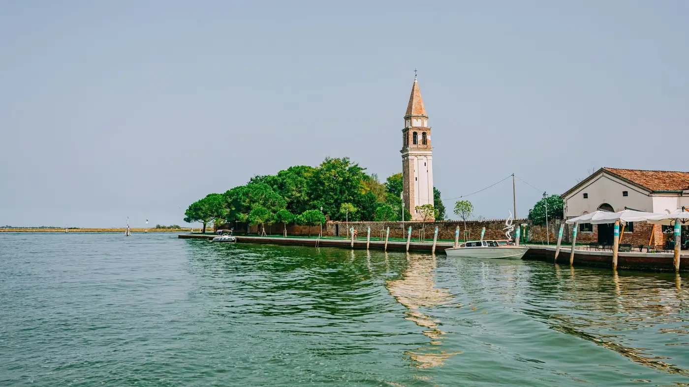 Picturesque island landscape showcasing the leaning bell tower of Burano, Italy, on a sunny day.