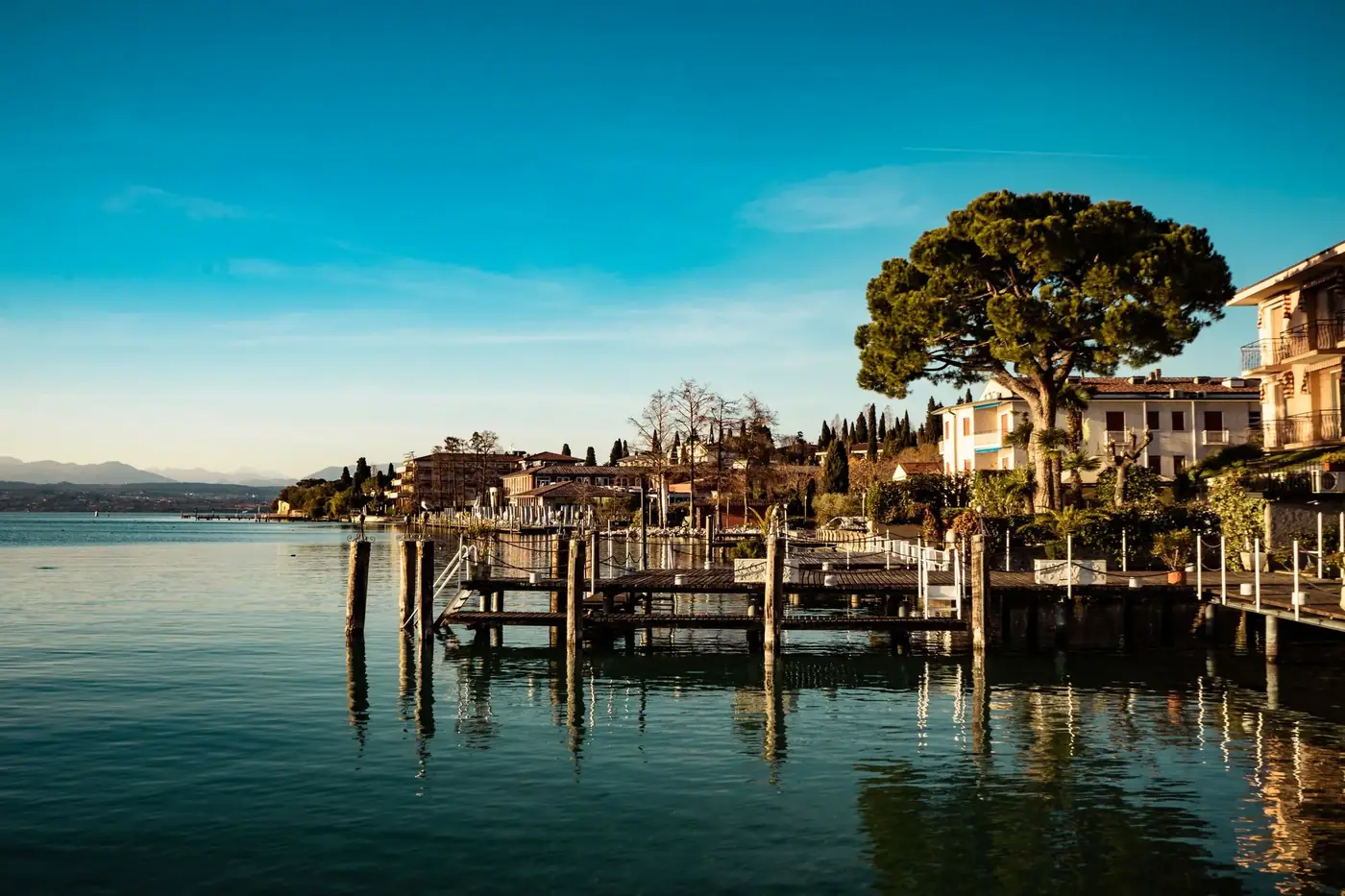 Beautiful waterfront town by a lake with reflections of buildings, trees, and a pier under clear blue skies.