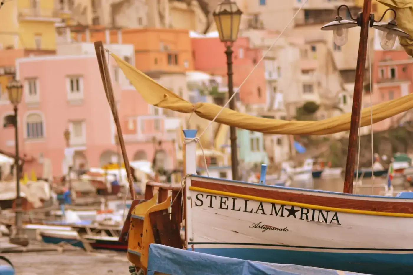 Vibrant boats docked at the charming marina in Procida, Italy, with colorful buildings and a warm atmosphere.