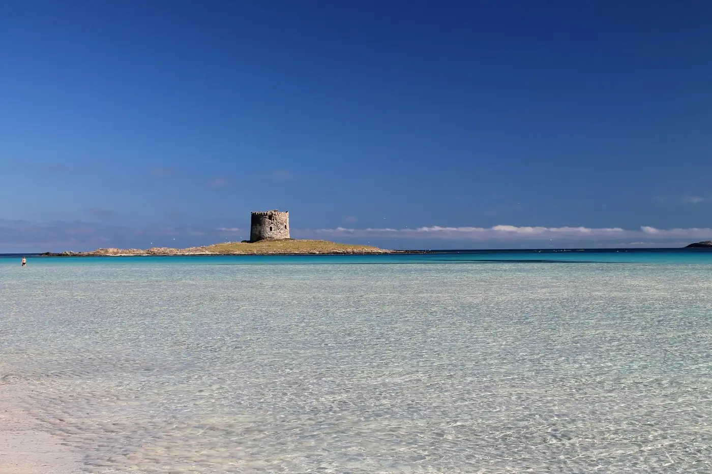 Panoramic view of Stintino Beach with azure waters and clear skies in Sardinia, Italy.