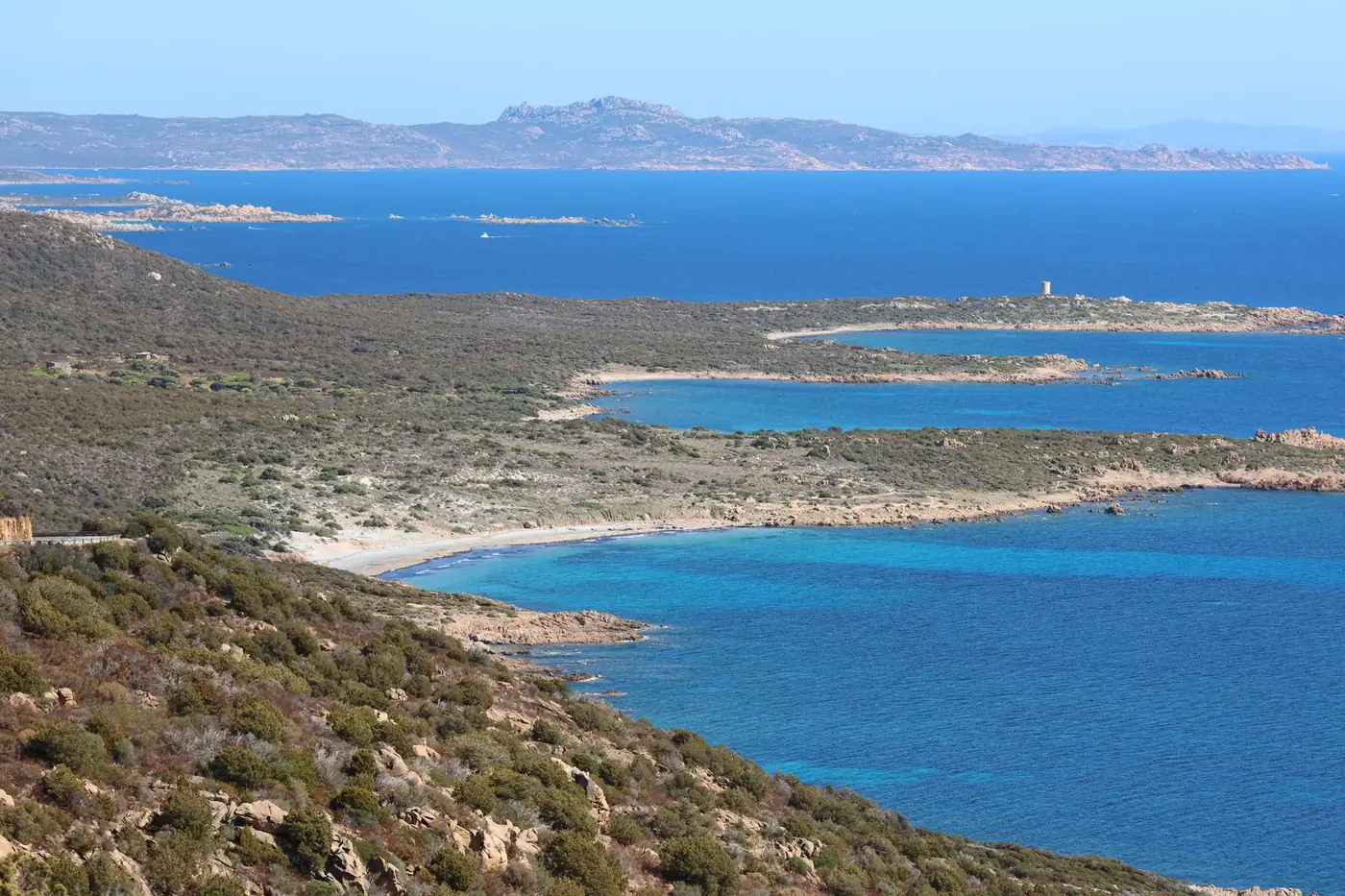 Breathtaking view of the Sardinian coastline with clear blue waters and rugged terrain under a bright day.
