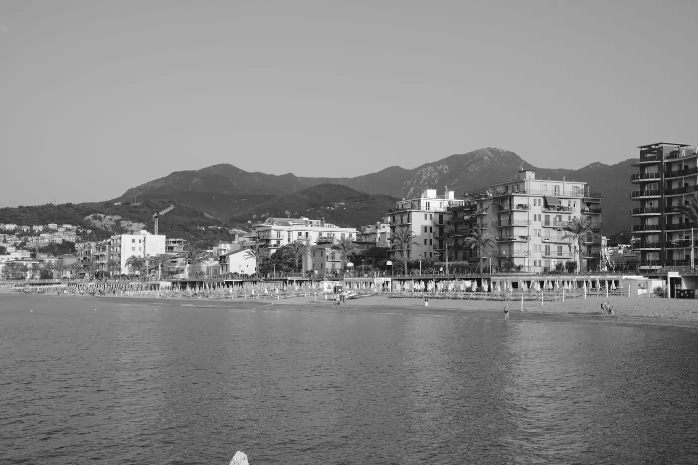 Black and white image of a picturesque seaside town in Italy with mountains and modern architecture.