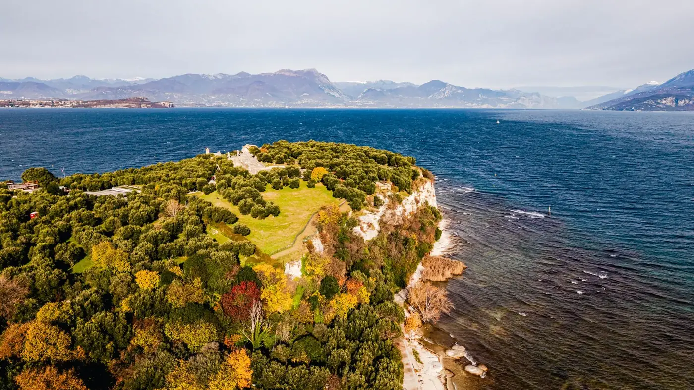 A breathtaking drone shot of the lush greenery and rocky shores of Isola del Garda, set against Lake Garda's vast blue e