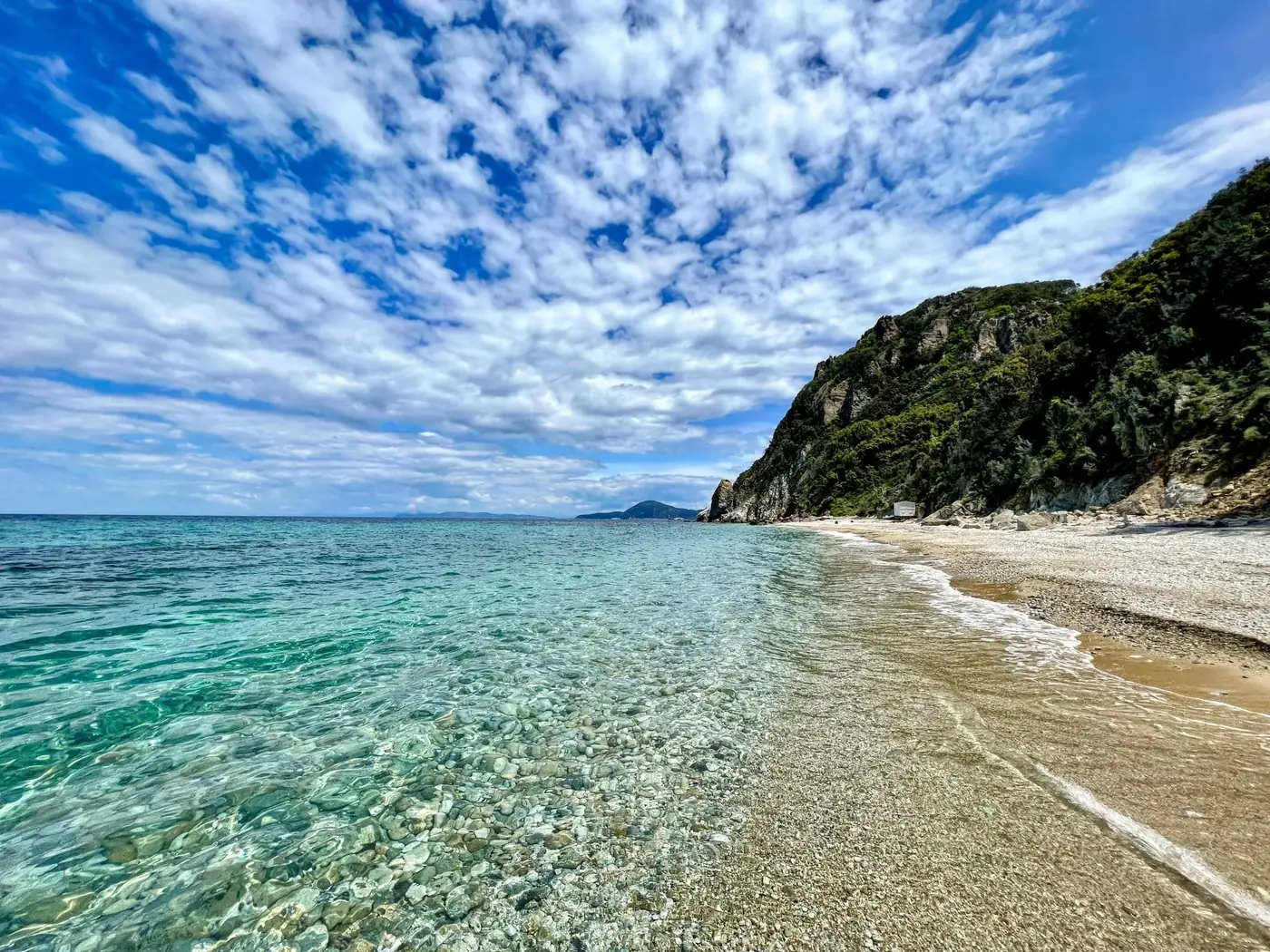 Stunning beach scene on Elba Island featuring clear blue waters and rocky cliffs under a vibrant sky.